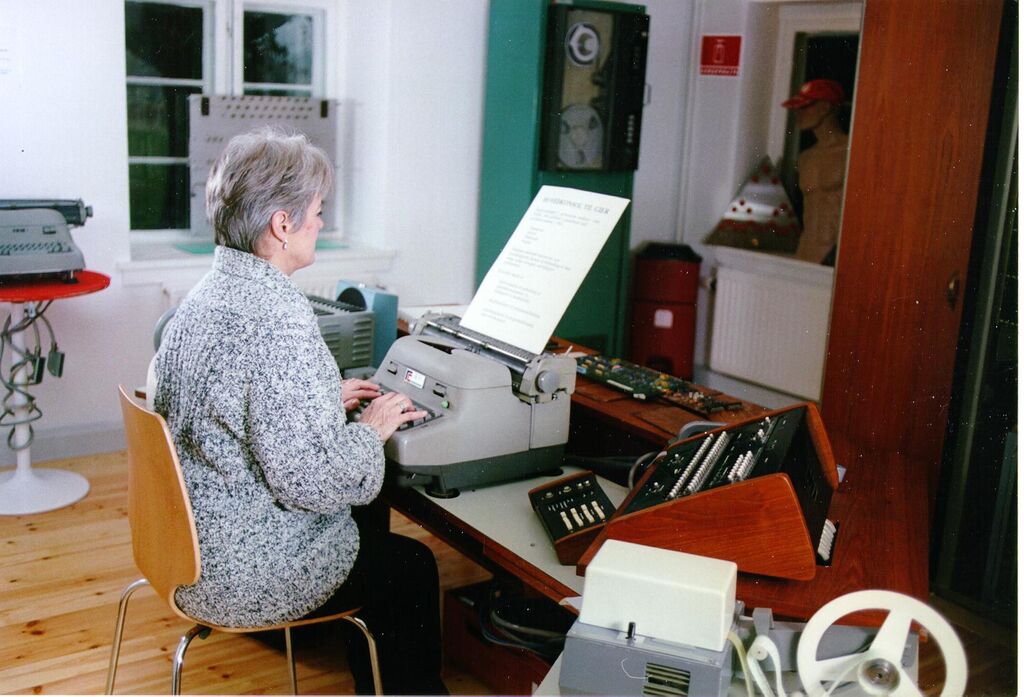 GIER. Selve maskinen tilhøjre bag trælåge. På bordet, forrest: perforator, kontrolborde, skrivemaskine og strimmellæser. I baggrunden en magnetbåndstation